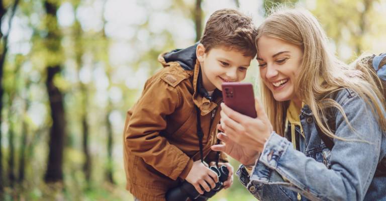Gelukkige moeder en zoon wandelen in het bos. Ze gebruiken kaarten op smartphones.